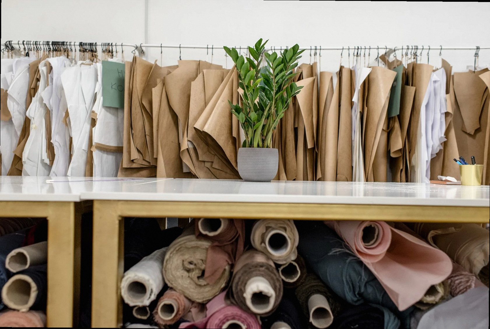 Rolls of various colorful fabrics and textiles stored under counter in front of rack with assorted sewing patterns for d
