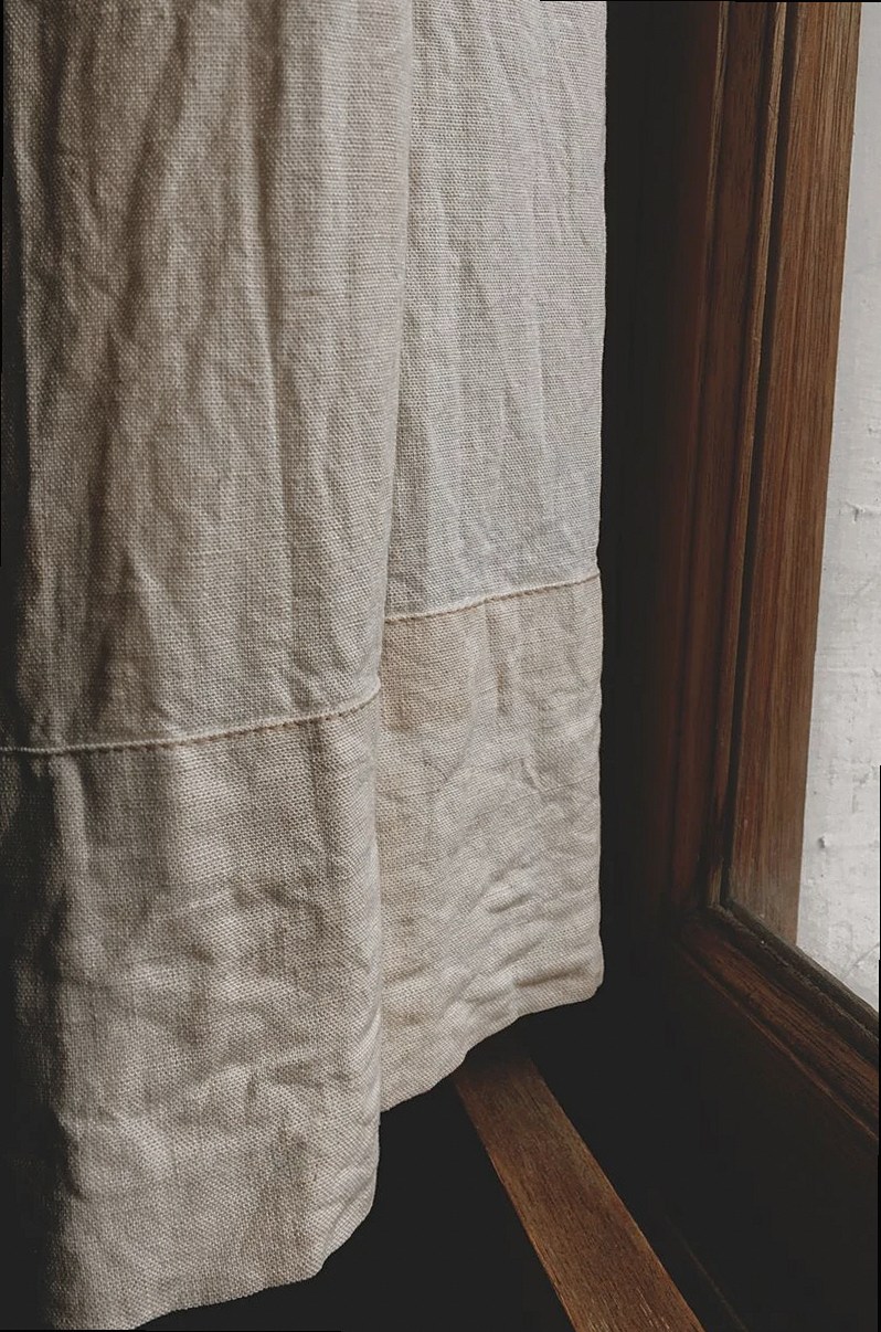 A detailed view of a textured curtain hanging beside a wooden window frame.